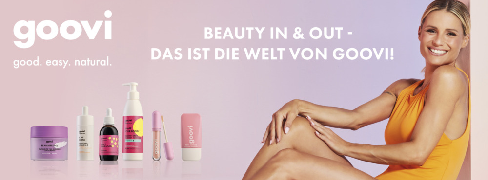 Werbeanzeige für die Marke Goovi: Eine lächelnde Frau in einem orangefarbenen Outfit sitzt vor einem pastellfarbenen Hintergrund. Links daneben sind verschiedene Goovi-Produkte in bunten Verpackungen aufgereiht, darunter Cremes, Seren und Lippenprodukte. Darüber steht der Schriftzug „goovi – good. easy. natural.“ und „Beauty in & out – das ist die Welt von Goovi!“.