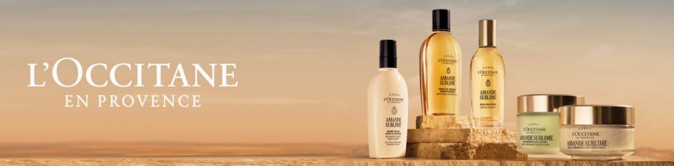 L'Occitane en Provence – Amande Sublime Kollektion mit Körperlotion, Duschöl, Körperspray und Körpercreme auf Naturstein vor Wüstenhintergrund