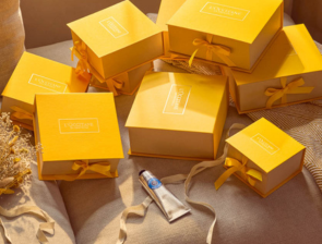 L'Occitane Geschenke – mehrere gelbe Geschenkboxen mit Schleife und Handcreme auf naturfarbenem Hintergrund