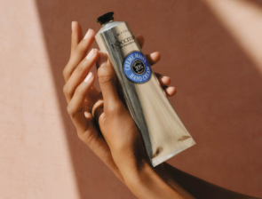 L'Occitane Karité Shea Butter Handcreme – Tube in Händen vor rosafarbenem Hintergrund
