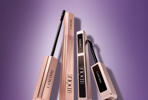Verschiedene Lancôme-Make-up-Produkte, darunter Mascara und Lippenstift, elegant arrangiert vor einem violetten Hintergrund.