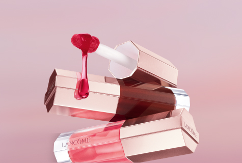 Drei glänzende Lip Idôle Juicy Treat Lipgloss von Lancôme in Rosé-Tönen, einer geöffnet mit tropfendem Applikator auf rosa Hintergrund.