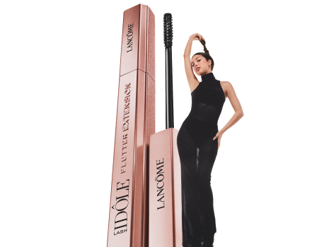 Lancôme Lash Idôle Flutter Extension Mascara in eleganter roségoldener Verpackung, neben einer stilvollen Frau in schwarzem Outfit.