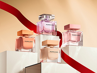 Vier quadratische Parfumflakons der Narciso-Reihe in zarten Farbnuancen wie Pfirsich, Nude, Rosa und Lavendel. Die Düfte stehen auf hellen Podesten, ein rotes Band zieht sich elegant durch das Bild.